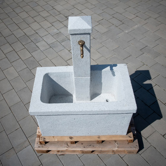 Marktbrunnen aus hellgrauen Stein mit einem guseiserenen Wasserhan für den Garten verkauft von Löseke´s Steingarten.